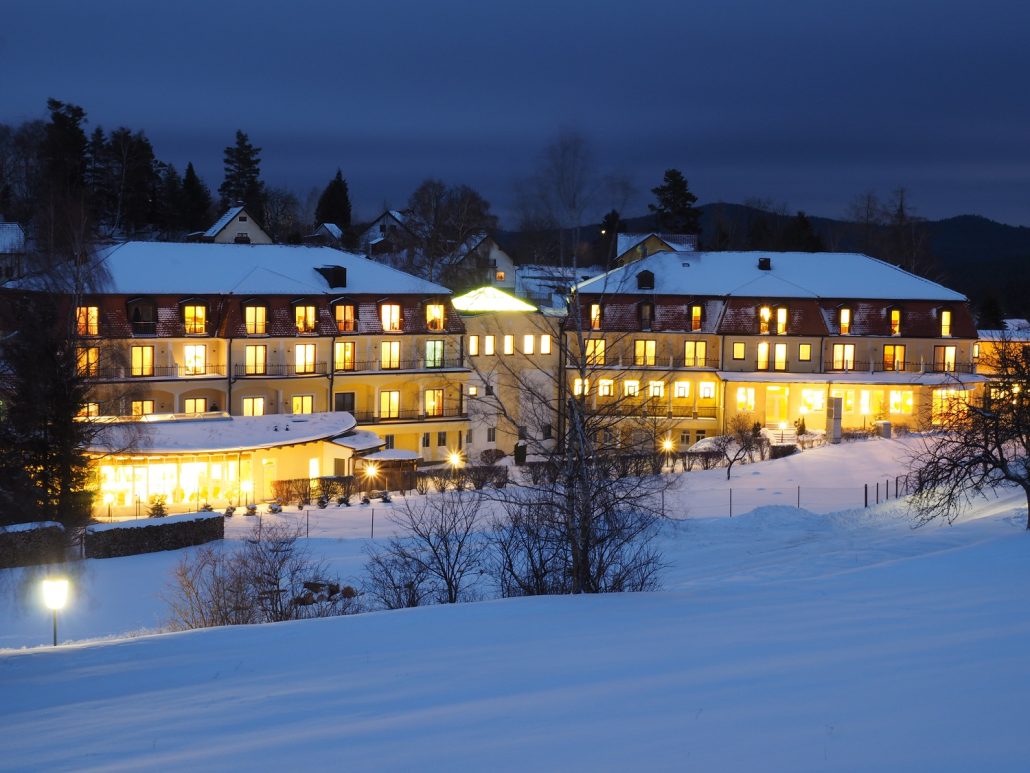 Klang & Moor - Moor Klang & moore Verschneites Hotel in der Dämmerung mit warm beleuchteten Fenstern, schneebedeckten Dächern und einer winterlichen Landschaft im Vordergrund.