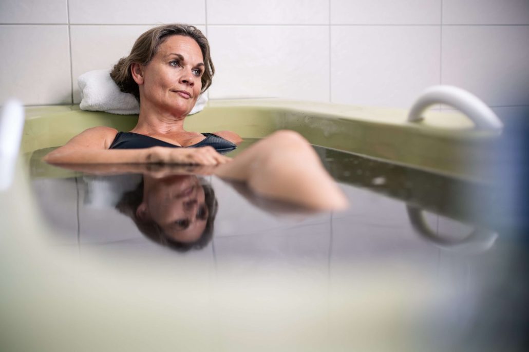 Moorbad Eine Frau entspannt bei einem wohltuenden Moorbad in einer Badewanne. Ihr Kopf ruht auf einem weichen Handtuch, während sie im dunklen Moorwasser liegt und die beruhigende Atmosphäre genießt.